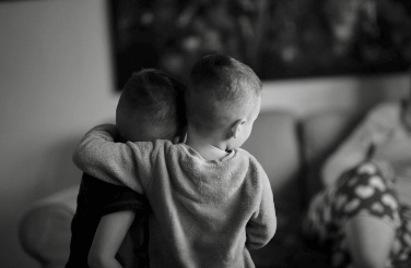 Two young children hugging each other with their backs to us
