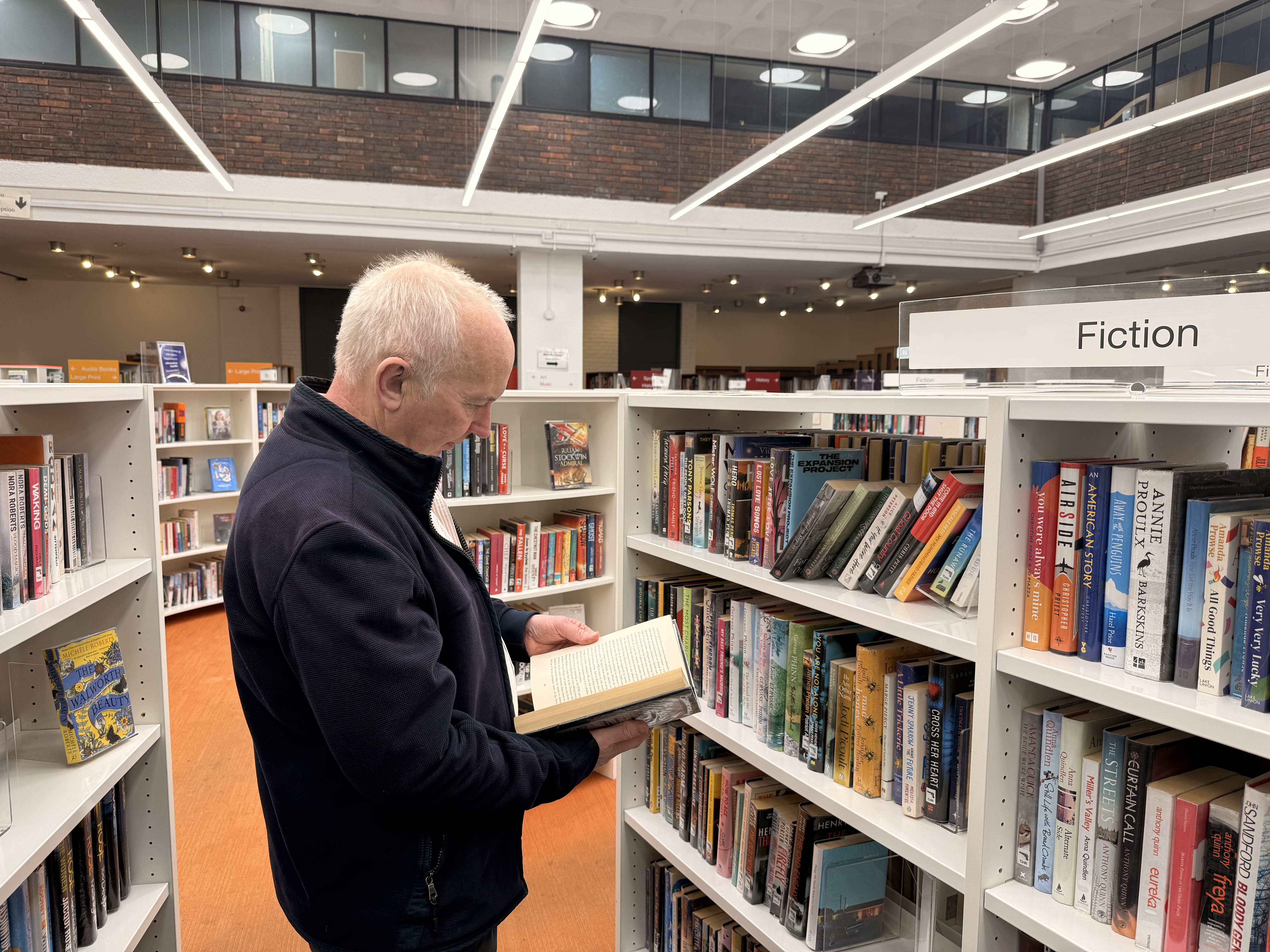 Councillor Barry Lewis, the Leader of Sutton Council standing in Sutton Library reading a book, standing by a book shelf.