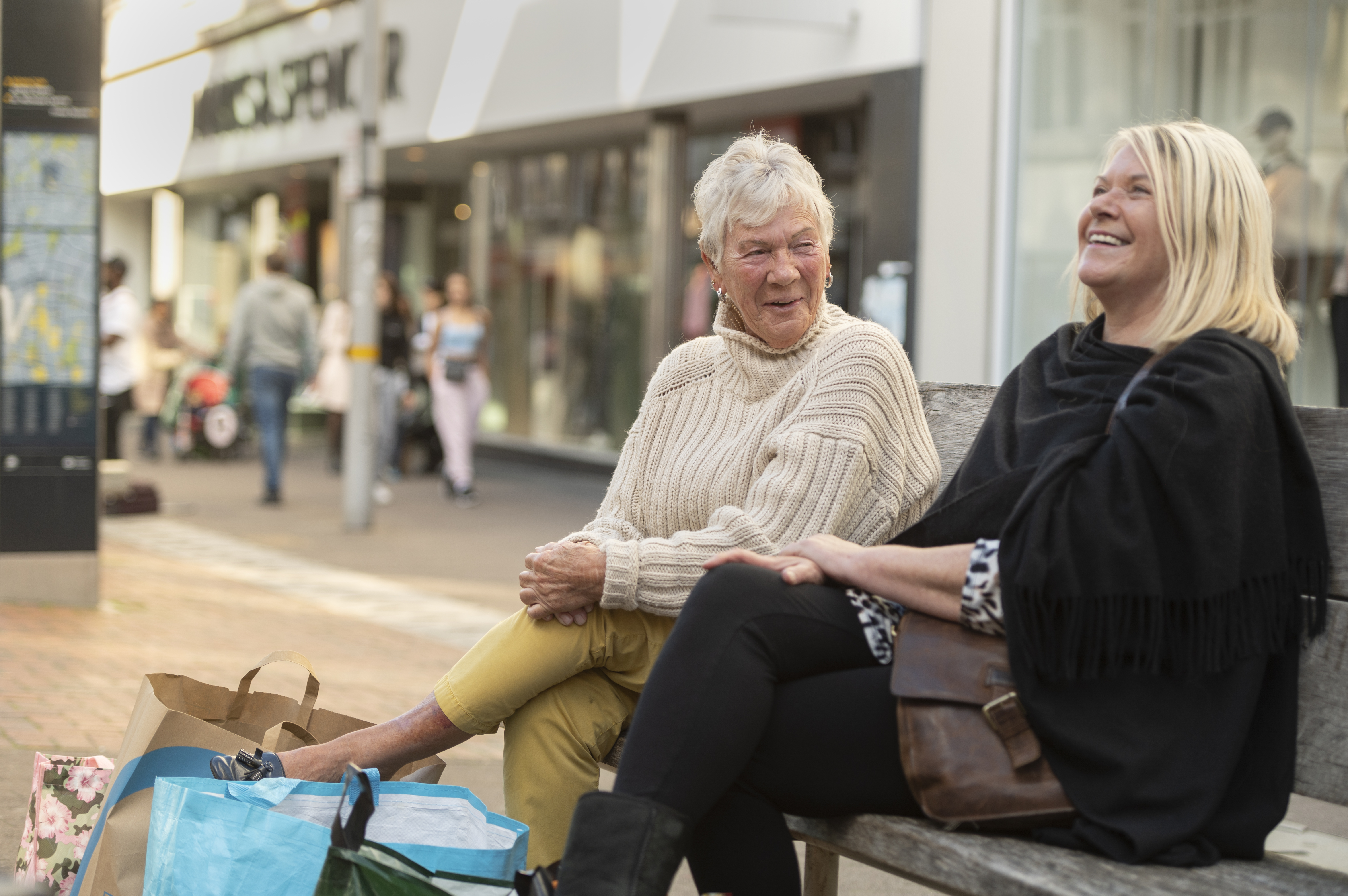 Two women sitting on a benching in Sutton highstreet laughing