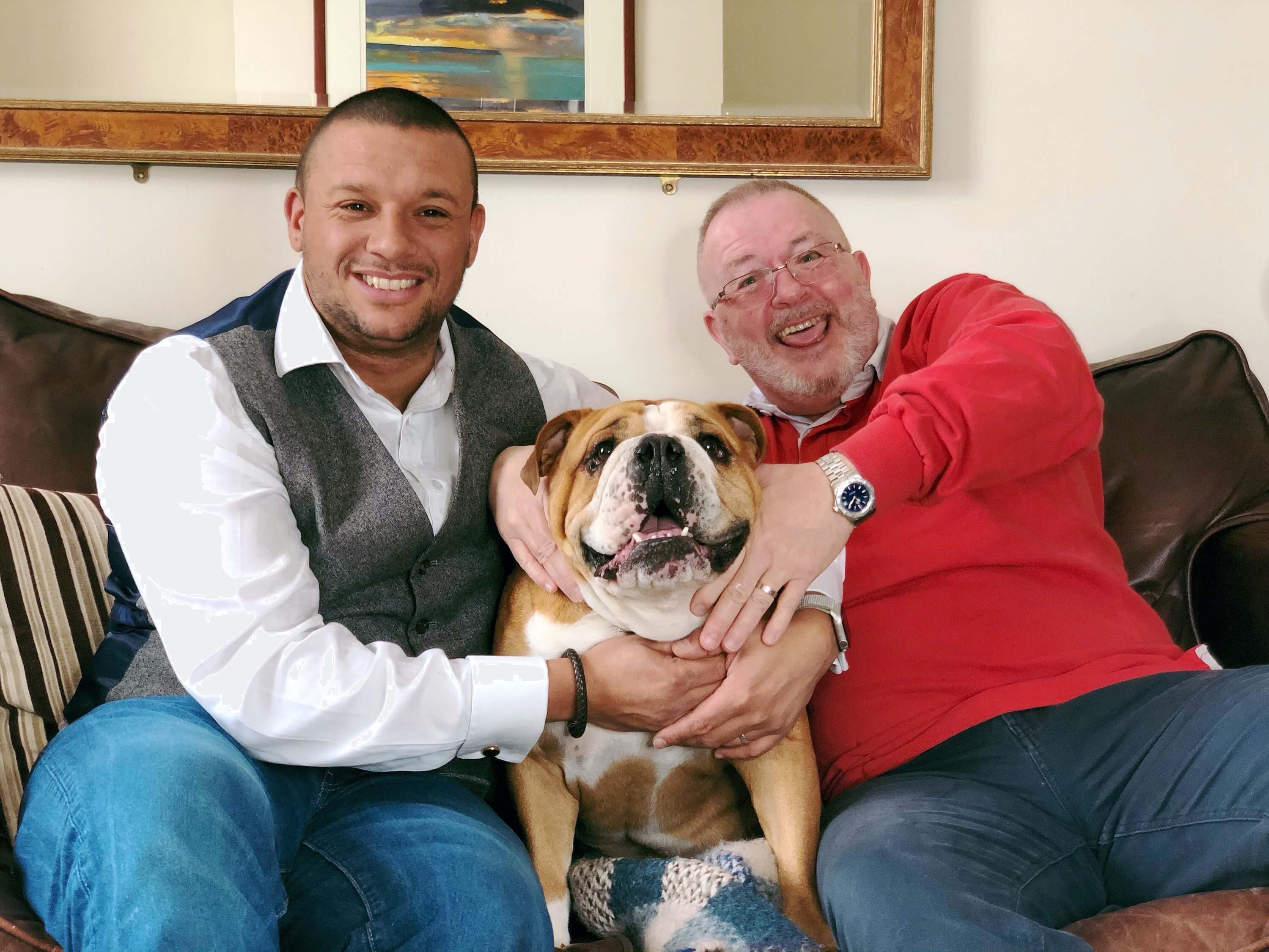 Two foster carers, Barnaby and Steven, sat on a sofa together with their bulldog.