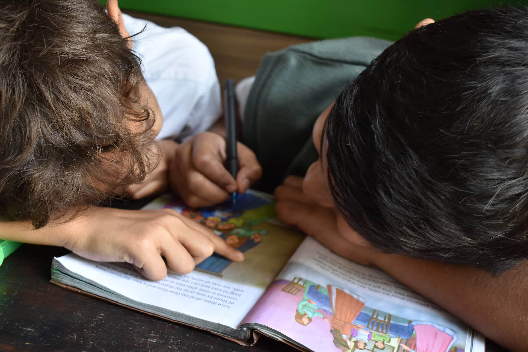 Two children bent over writing in a book together.