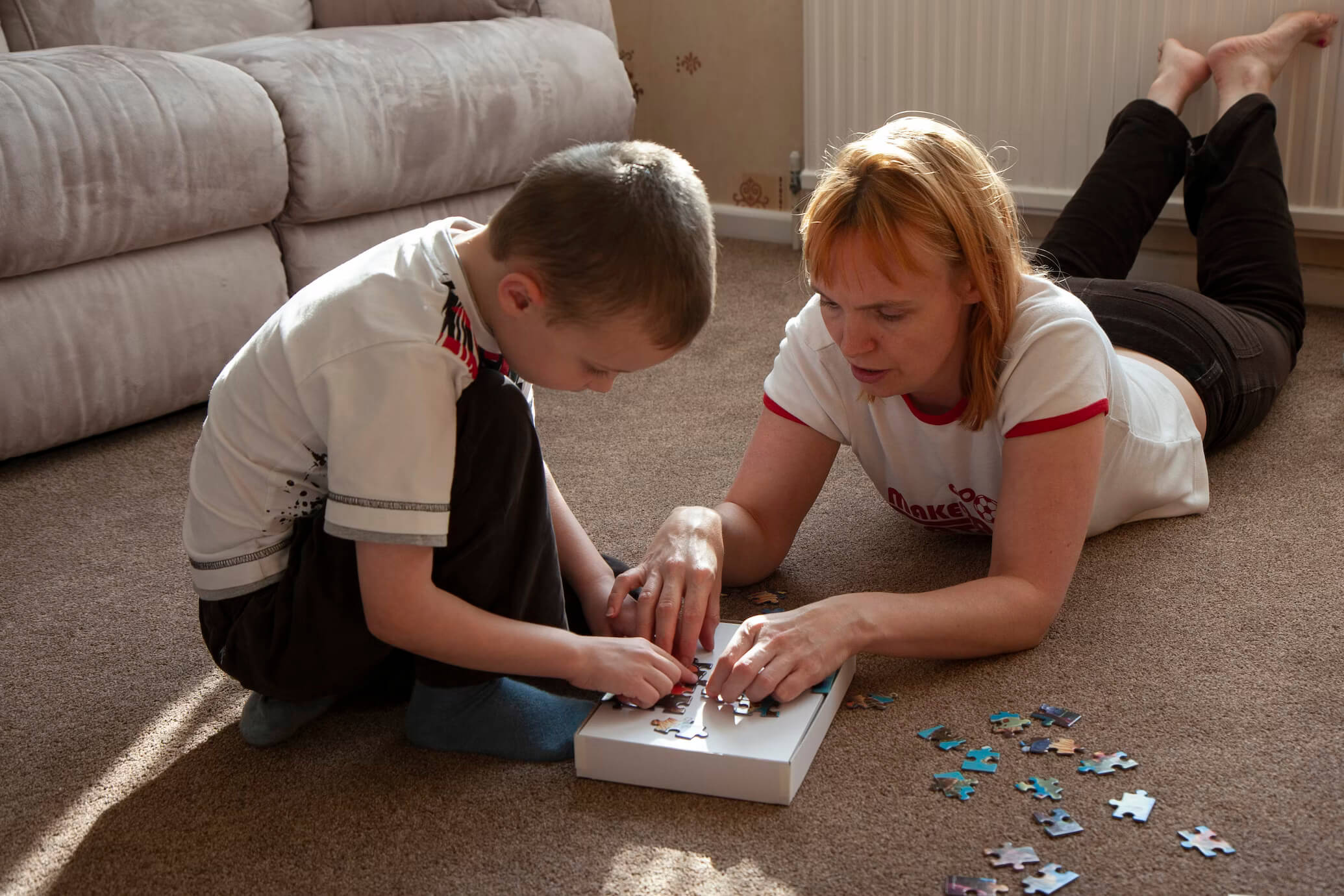 Woman and a young boy sat on living room floor together completing a puzzle.