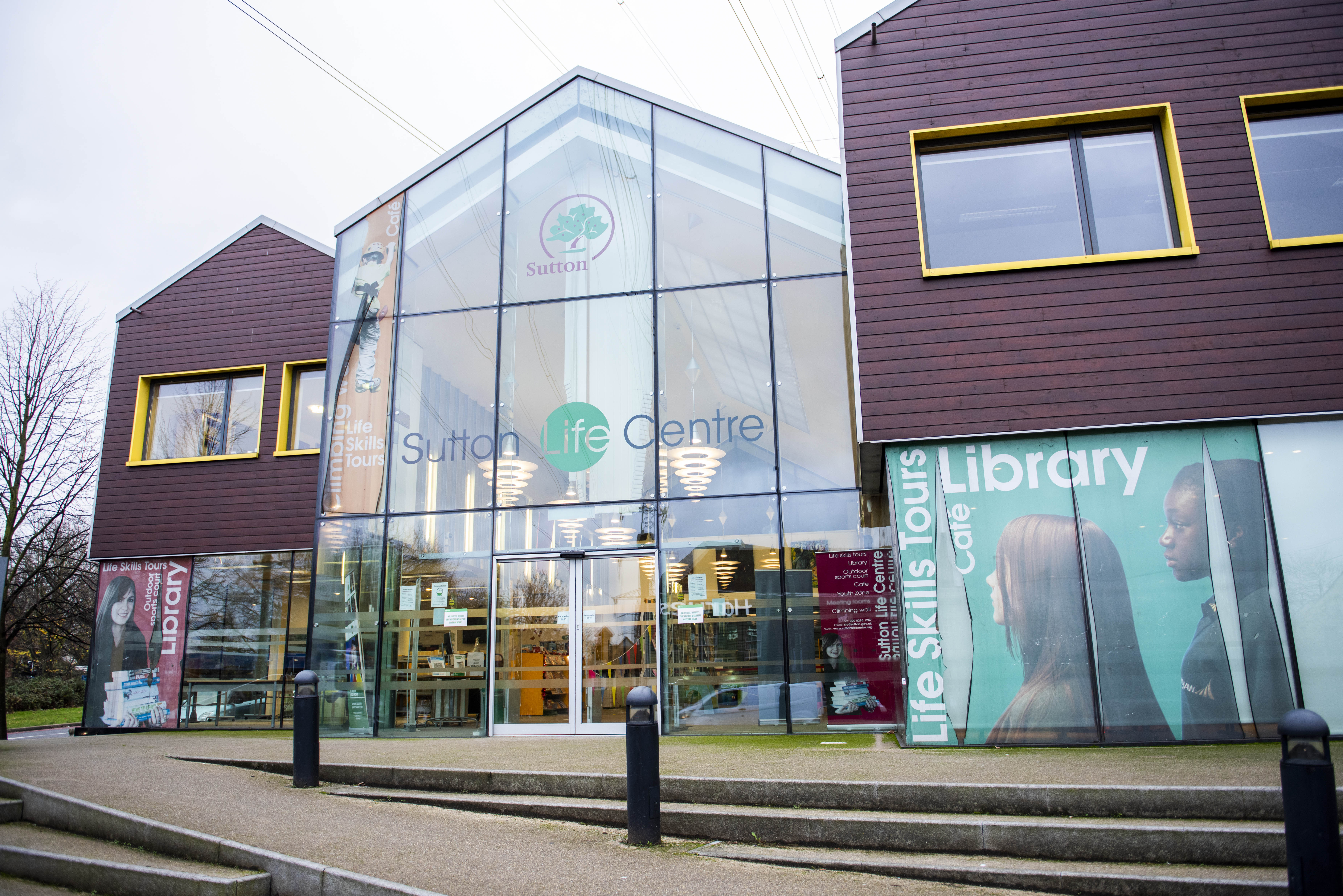 Photograph shows the front entrance to the Life Centre which has a tall glass frontage, which says Sutton Life Centre high up on the glass