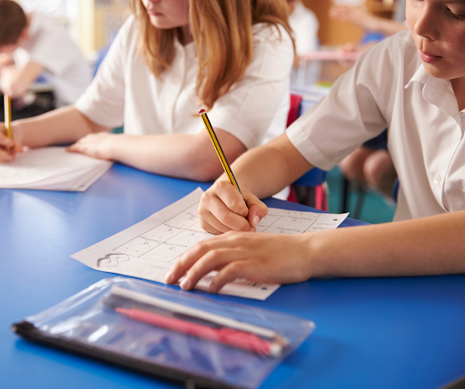 Close up of children in school uniform sitting at desks with pencils in hand, writing