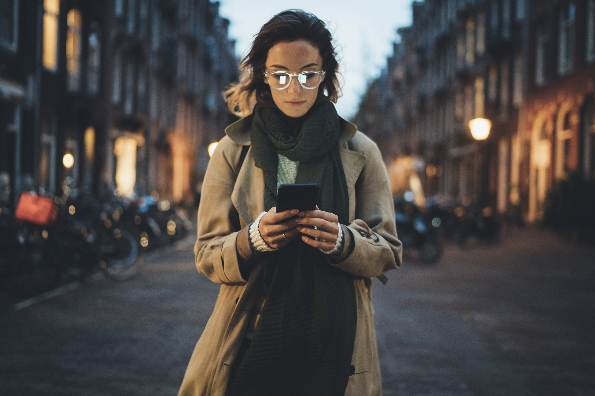 Image shows a London street scene at dusk with a young woman walking along looking at her mobile phone